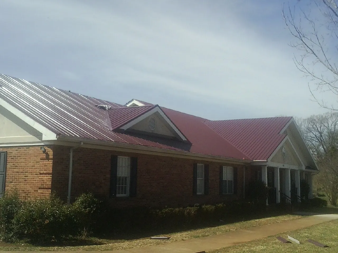 Red metal roof with gabled entries on a long brick building, from a Hail Damage Roof Repair job in El Dorado Hills