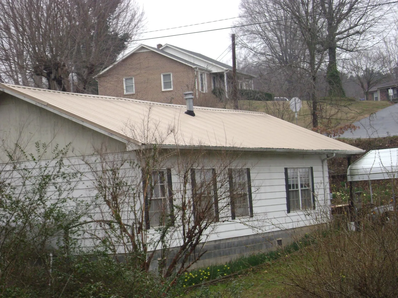 Tan metal roof on a white sided house set into a hillside — Commercial Roofing by Roofing Brothers in El Dorado Hills